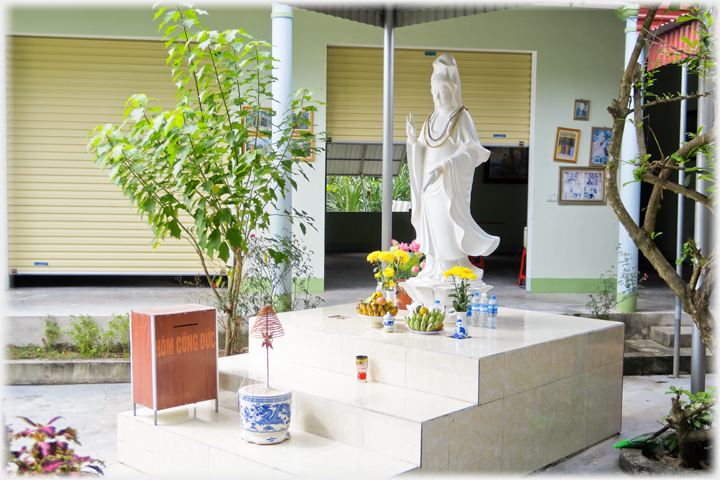 White Buddha on white plinth with box and incense on lower step.