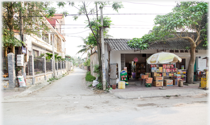 A lane running off the road with a corner shop stacked high with goods outside.