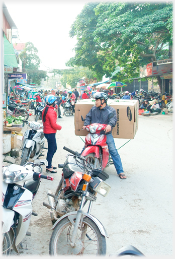 Motorcyclist talking to woman with washing machine on the back of his bike.