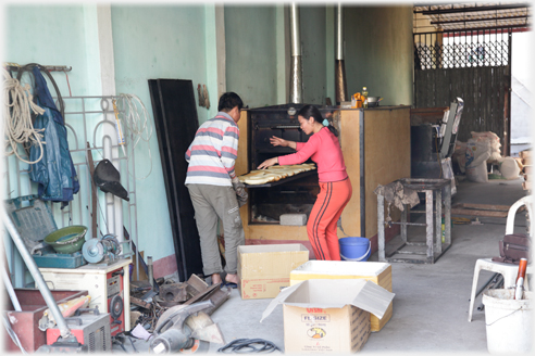 Two people checking a shelf of bread pulled from the large oven.