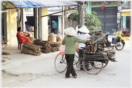 Women with bicycles laden with bundles of trimmed firewood.