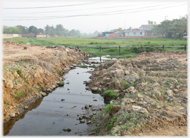 Rough ground with large ditch and fields beyond.