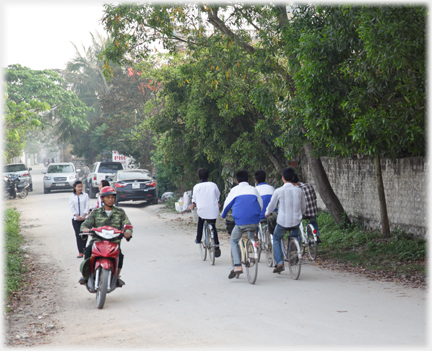 School children, motor cyclist and cars on the road at the south end.