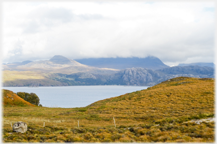 View across loch with fissured crags and tiny houses.