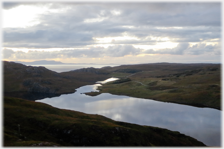 Foreground loch with sea and mountains beyond.