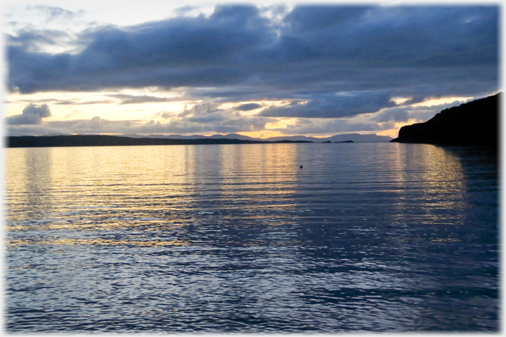 Sunset across sea with mountains on horizon.