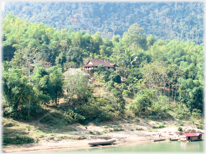 House amongst trees with boats and house boat at river bank below.