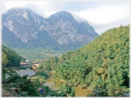 Houses on one side of a tributary, trees on the other and a karst beyond.