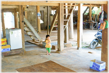 A small child standing in the middle of the area under the house trying to fold its arms.