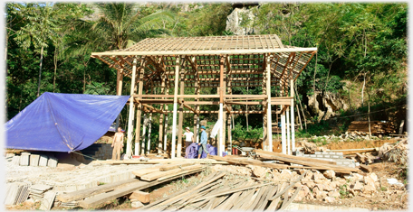Wooden skeleton of Thai house with workers and piles of wood.