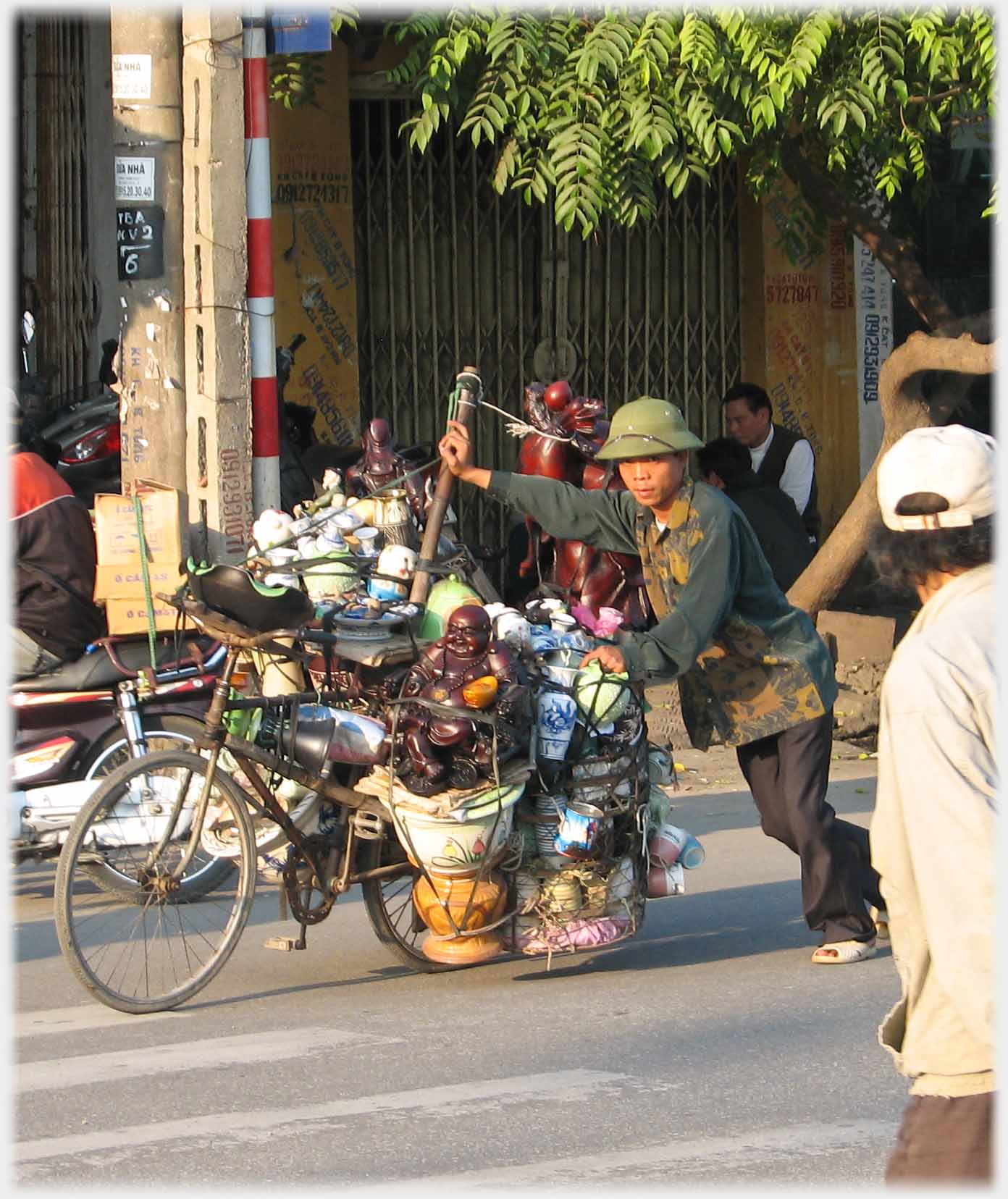 Man leaning hard into pushing his heavy load of ceramics on a bike, using a pole extension.