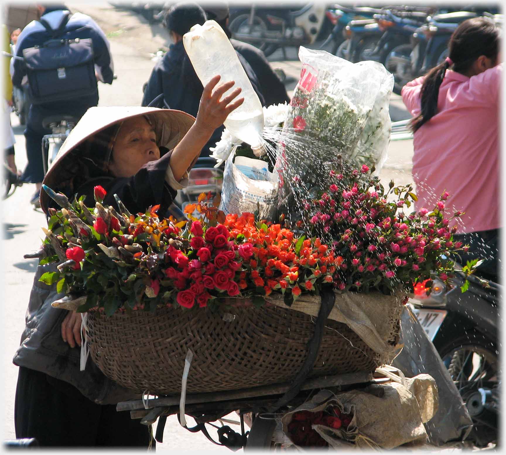 Woman in conical hat shaking bottle of water over flowers.