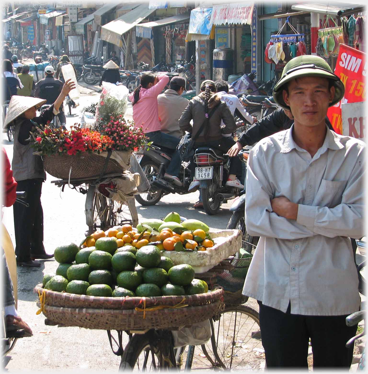 Man standing square on looking at camera beside fruit on bike.