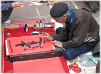 Man writing Chinese charaters sitting on the ground.