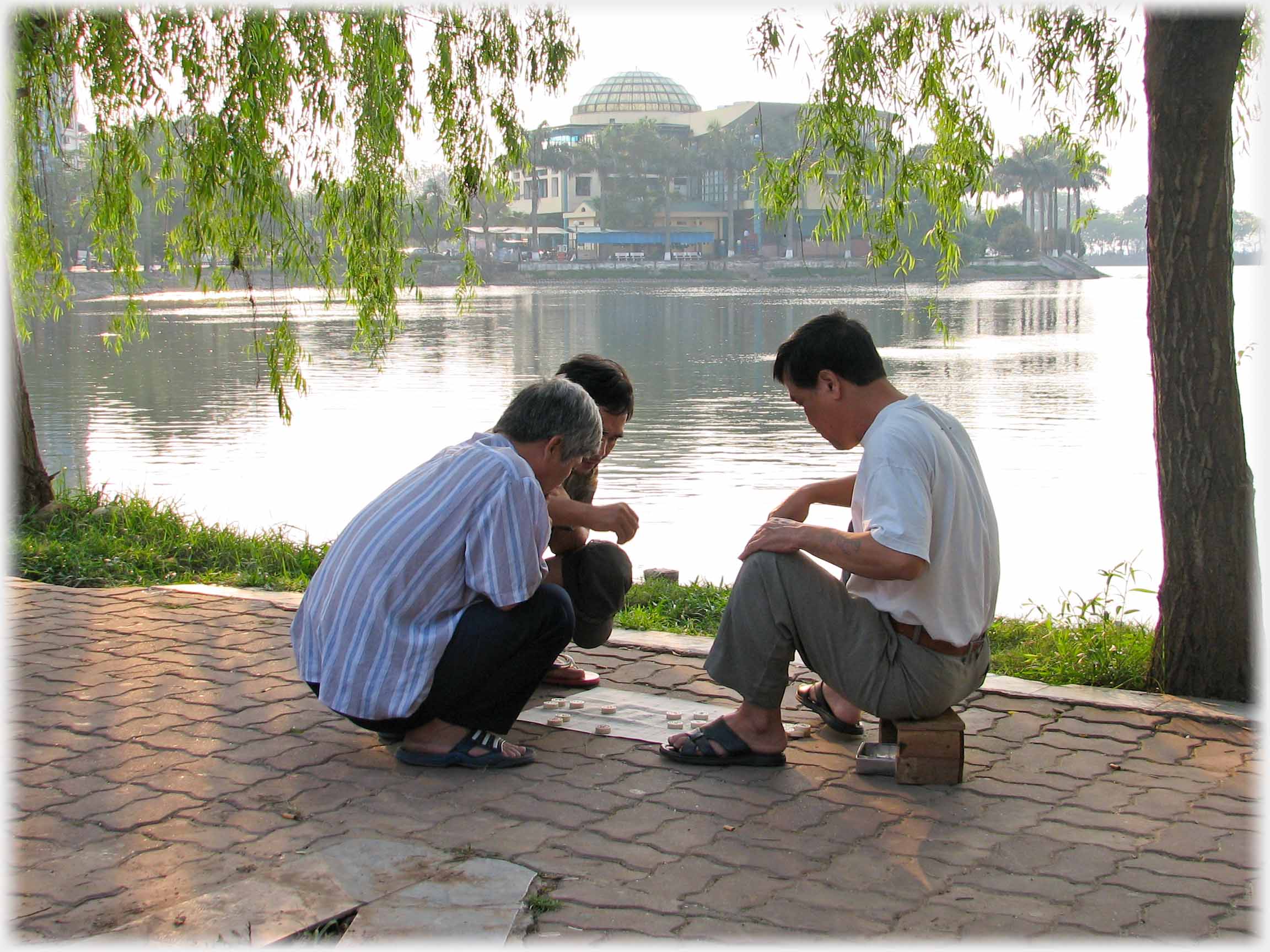 Three men and paper 'board' by lake, one on small stool.