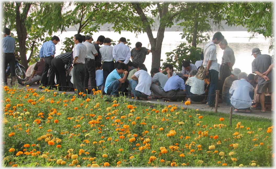 Group of thirty or so men standing and sitting, lake in background.