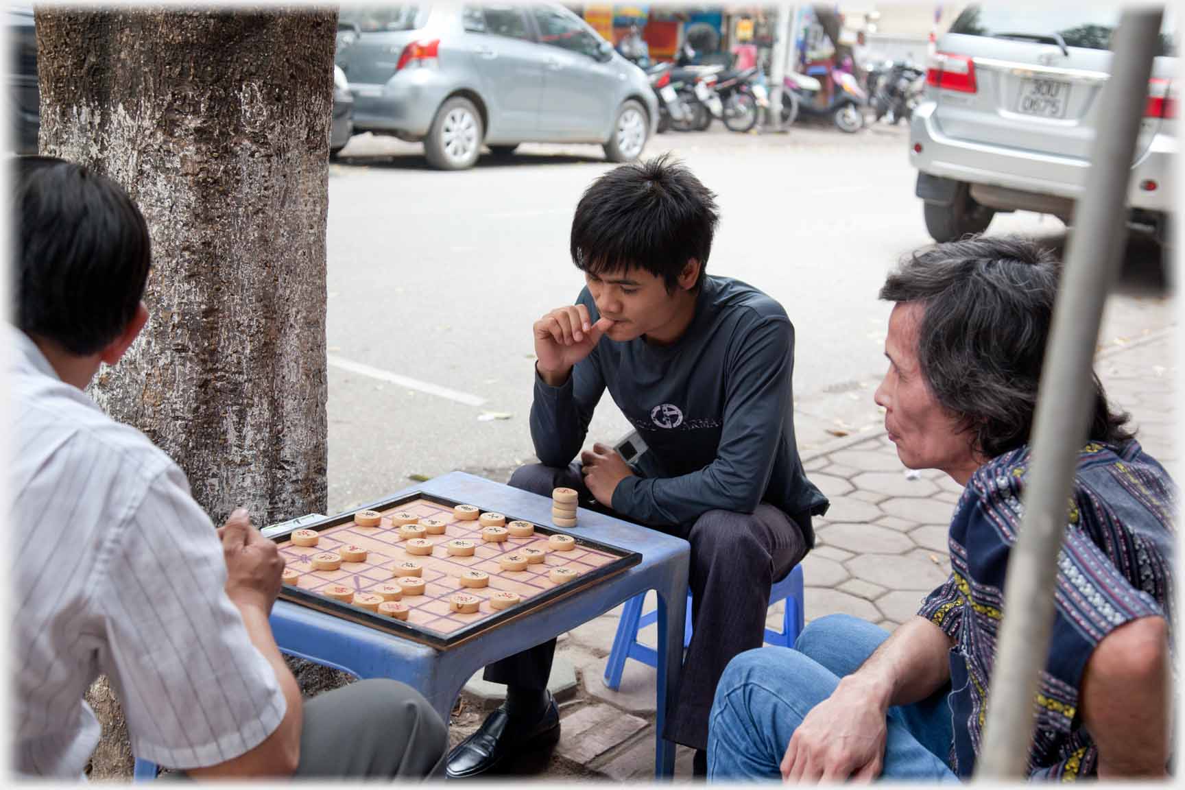 Three men sitting on stools around table with game in progress.