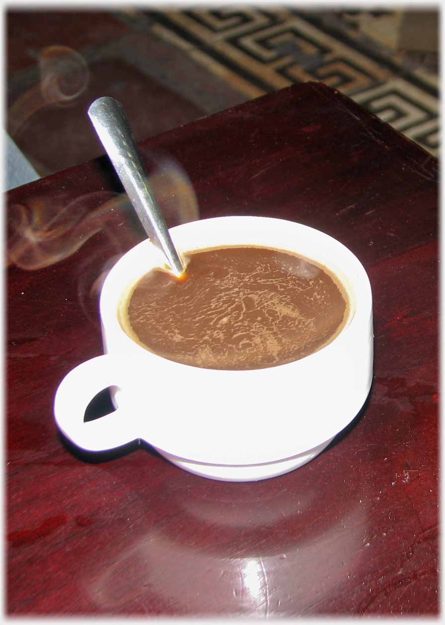 Small dark brown coffee with teaspoon and steam.