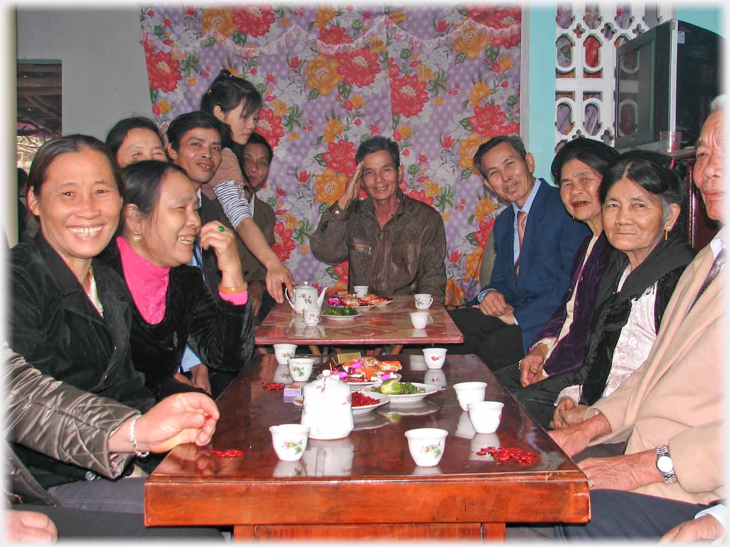 Group sitting on either side of reception table in house with tea cups.