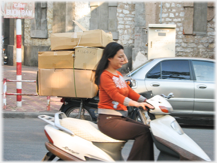 Elegant woman on up market motorbike with boxes on bike behind her.