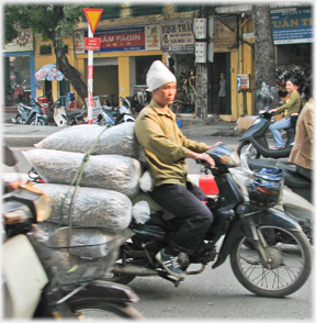 Curious cloth hat on man with cylindrical bundles.