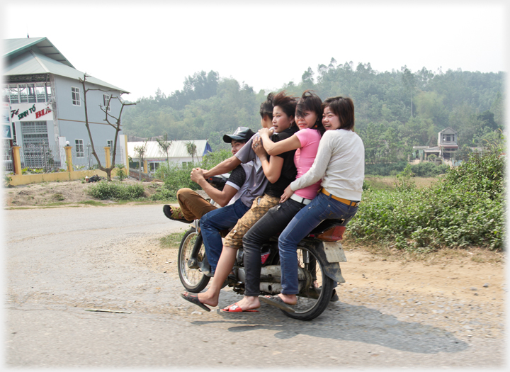 Man driving bike with three female and one male passenger.