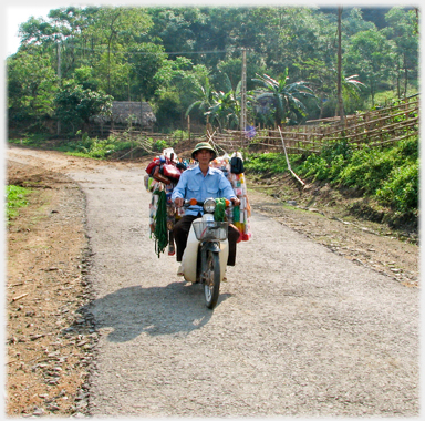 Man on country road with items hanging behind him.