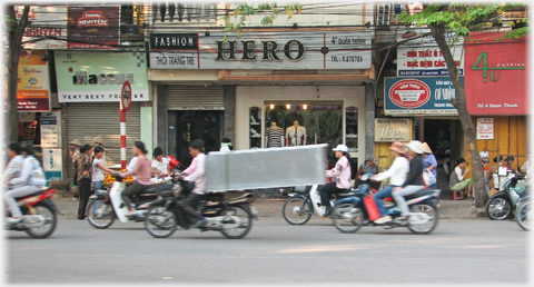 Moving traffic with very long rectangular box strapped to pillion seat and extending behind for the length of another bike.