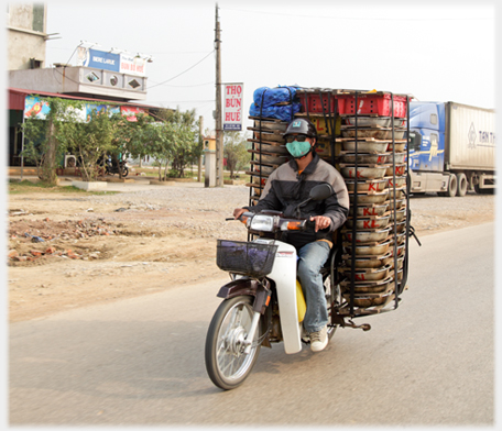 Man riding on open road with flat trays stacked behind him.