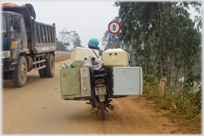 Motorbike with machines strapped to either sidde and on top, lorry on other side of road, 5 ton weight limit.