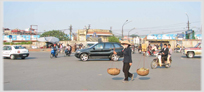 Woman walking across large road intersection with passing bikes and cars.