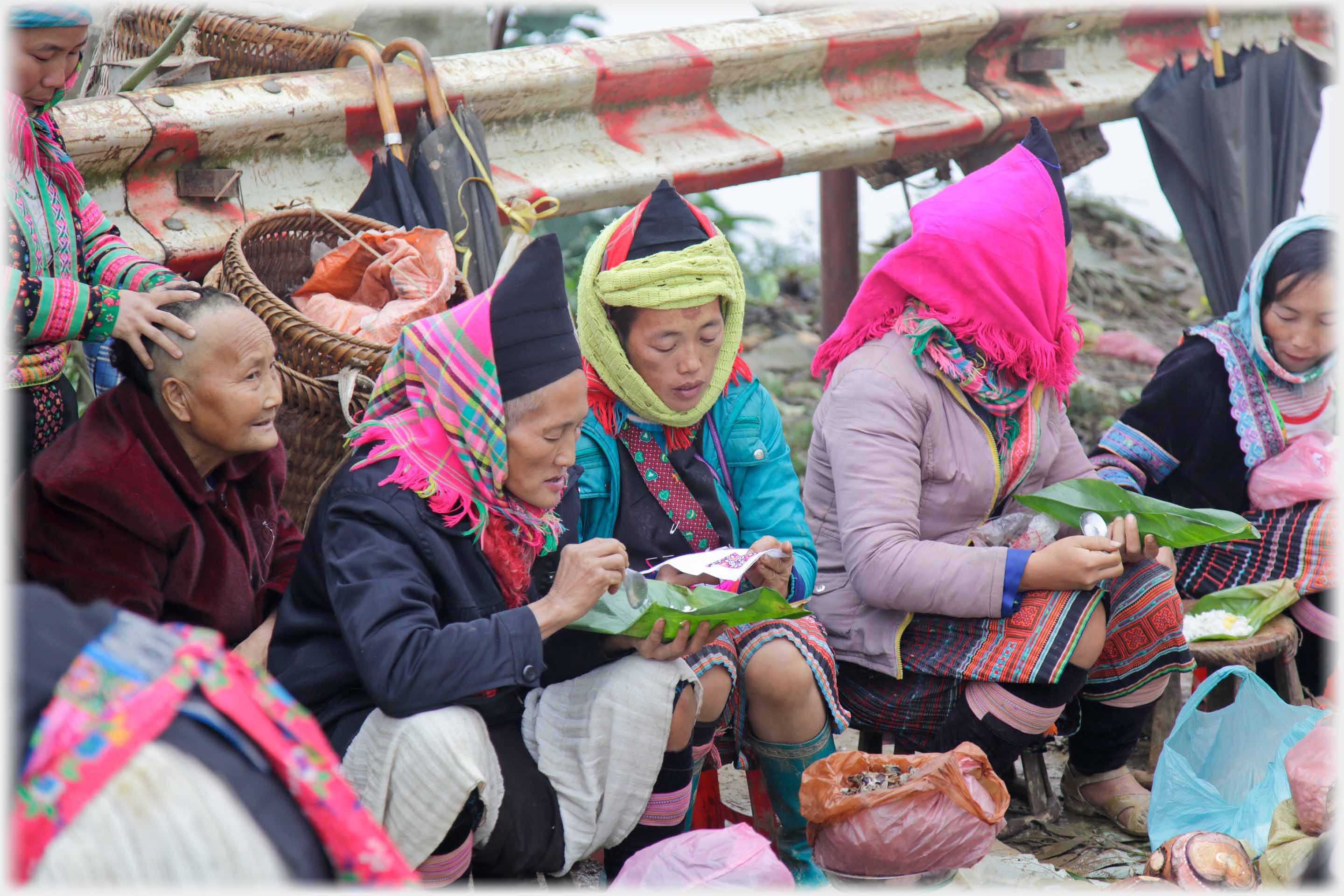 Group of women eating from banana leaves, one have head massage.