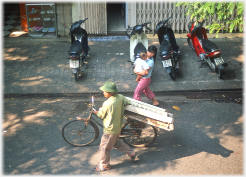 Man walking with large object on the saddle of his bike.