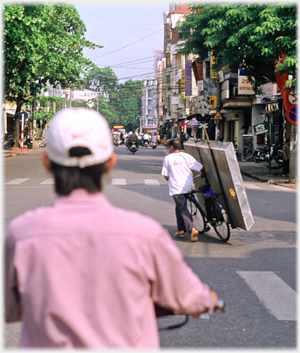 Man wheeling bike with frame holding a matress.