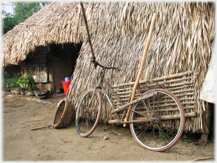 Bicycle with poles attached leaning against a thatched house.