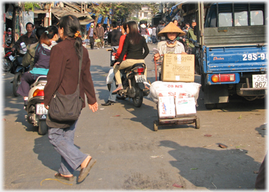 Behatted woman with loaded sack truck.