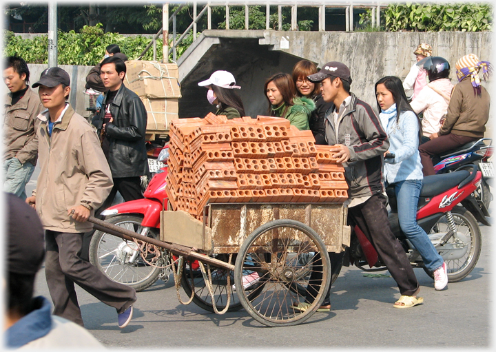 Small cart loaded with bricks being pulled and pushed through traffic