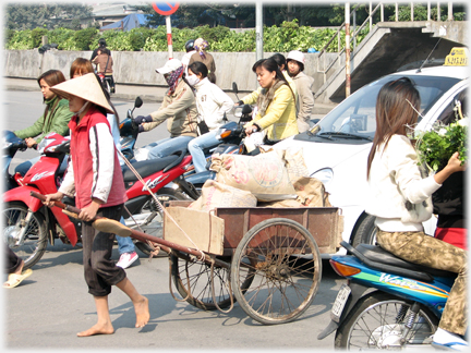 Woman pulling cart in hat surrounded by traffic.