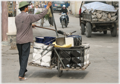 Man guiding heavy load of ceramics with poles attached to his bike.