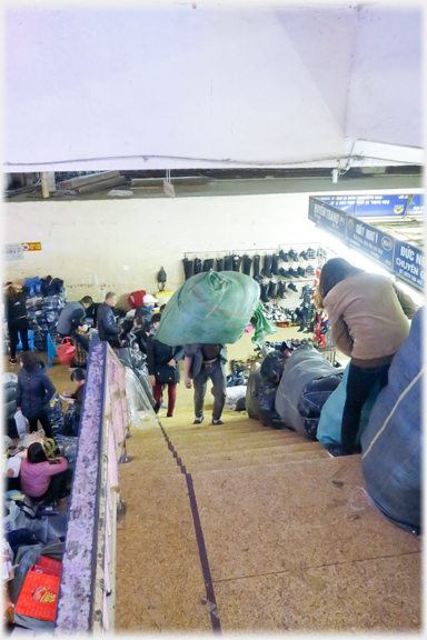 Man ascending stairs under enveloping bundle. Other bundles on steps.