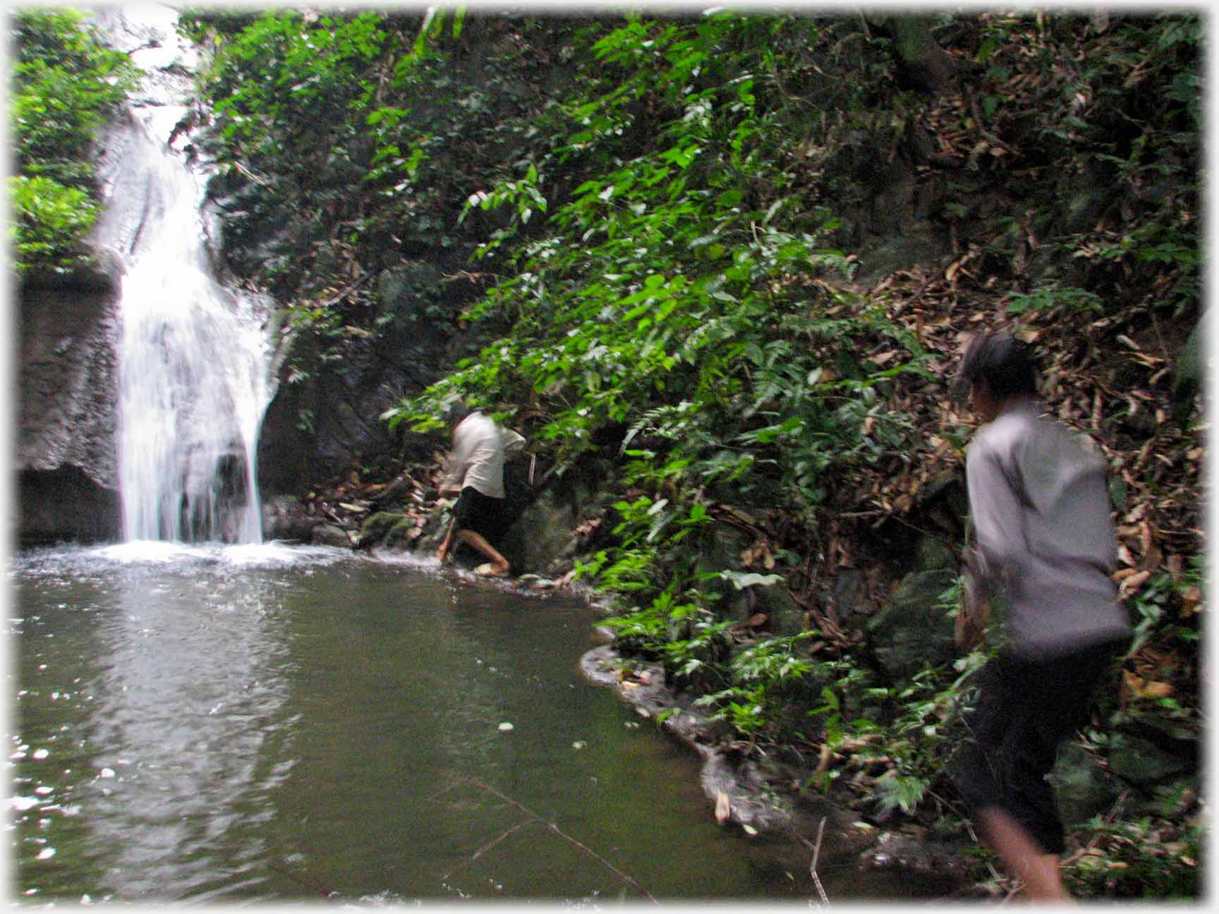 Waterfall entering pool, two figures along edge of pool.