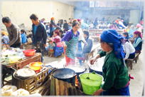 Women making food, tables of eaters in background.