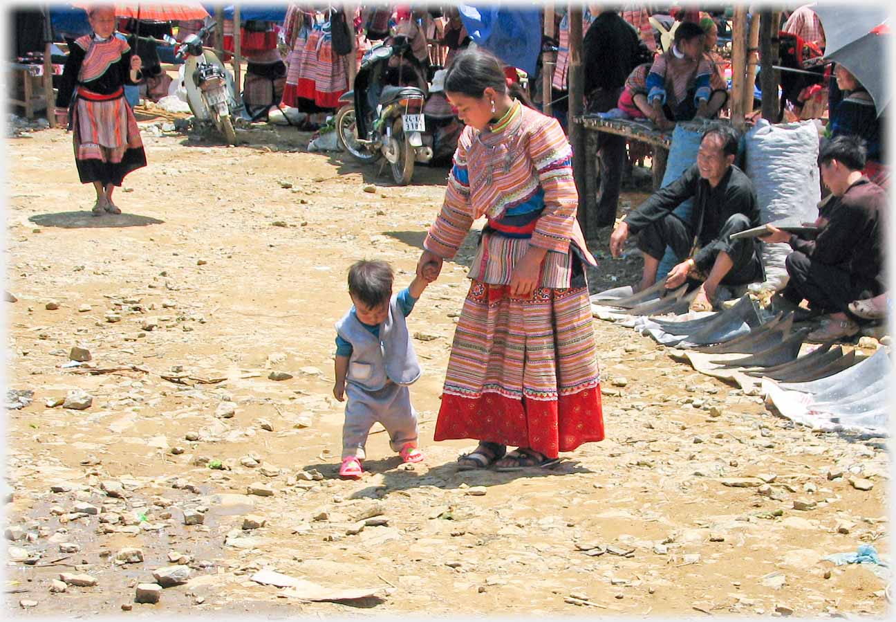 Woman walking with infant looking at stoney ground.