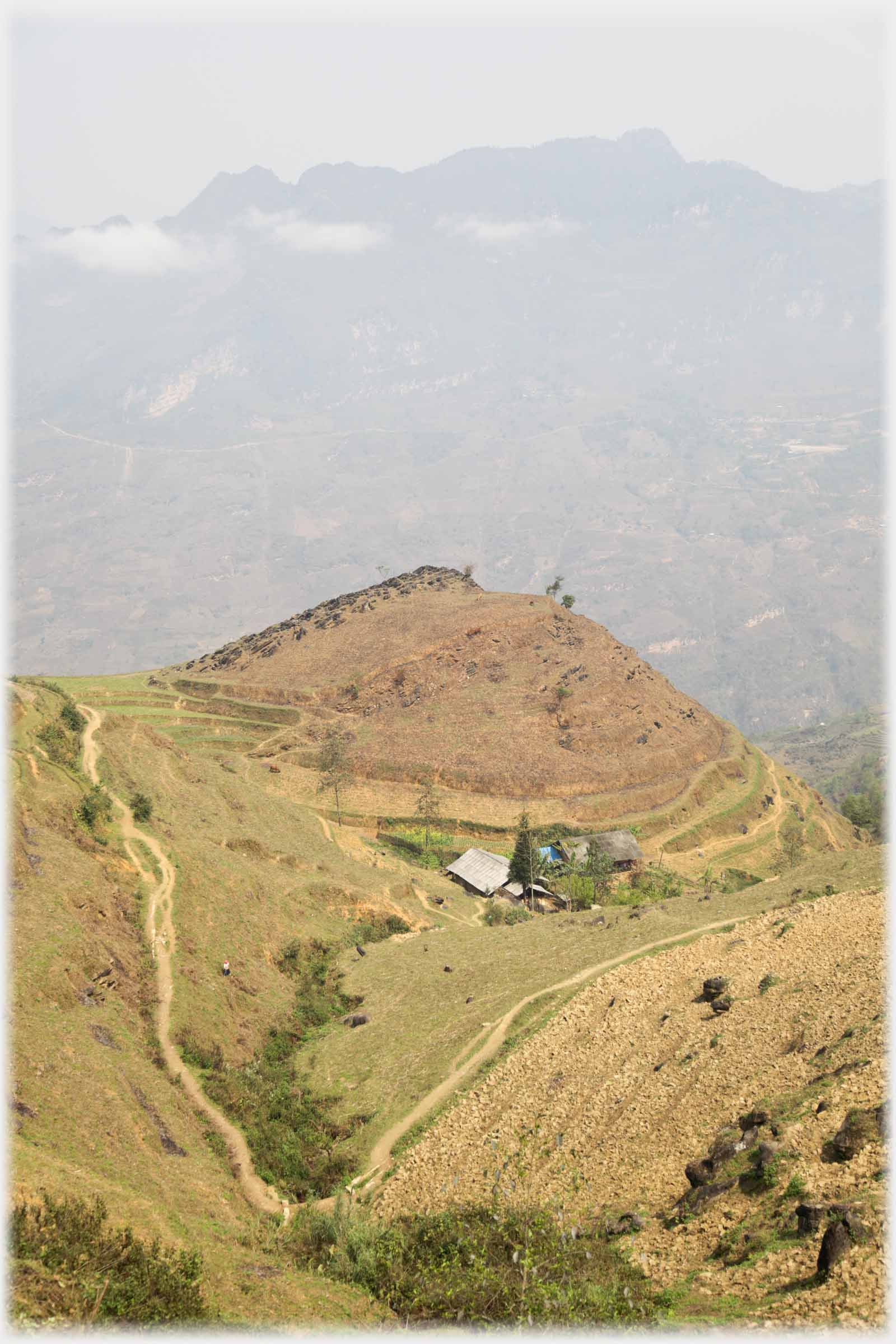 Conical hill with house at bottom on neaer side, mountains beyond.