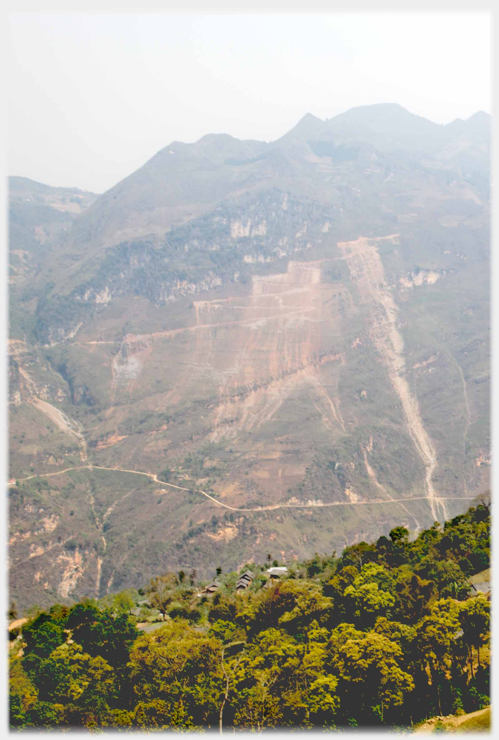High vertical hillside with streaks of falling earth down below road.