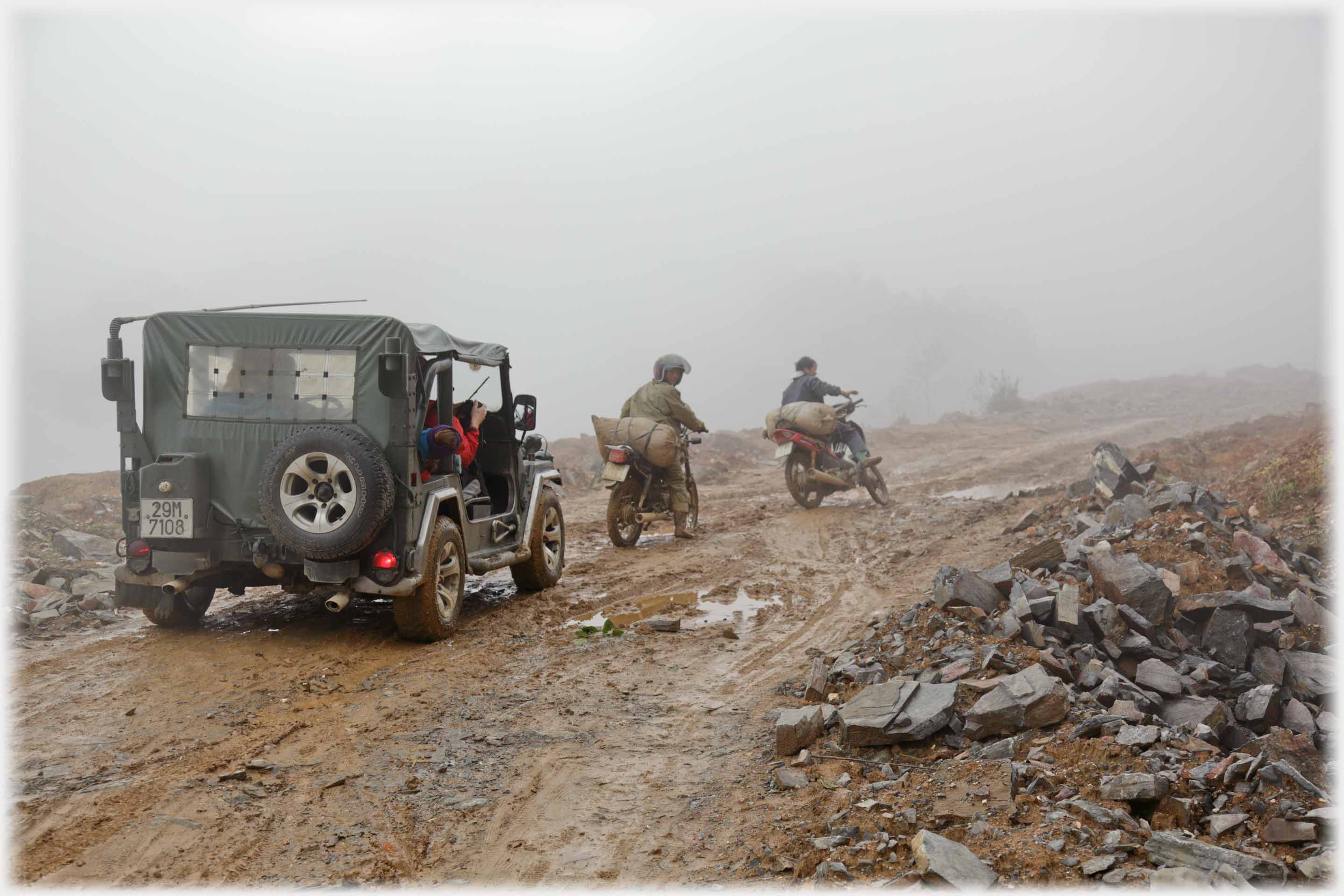 Jeep behind two motorbikes going towards mist.