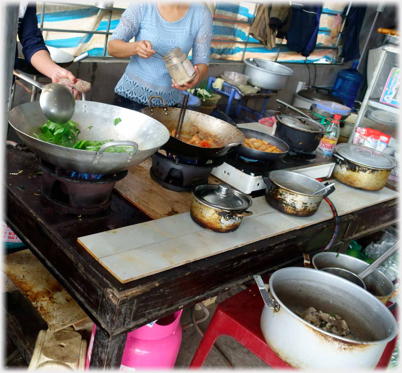 Table with gas cylinder under and gas burners, woks and pots on top.