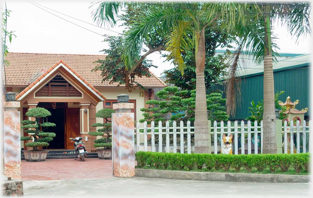 Single story house entrance with bonsai, fence and plastic dog.