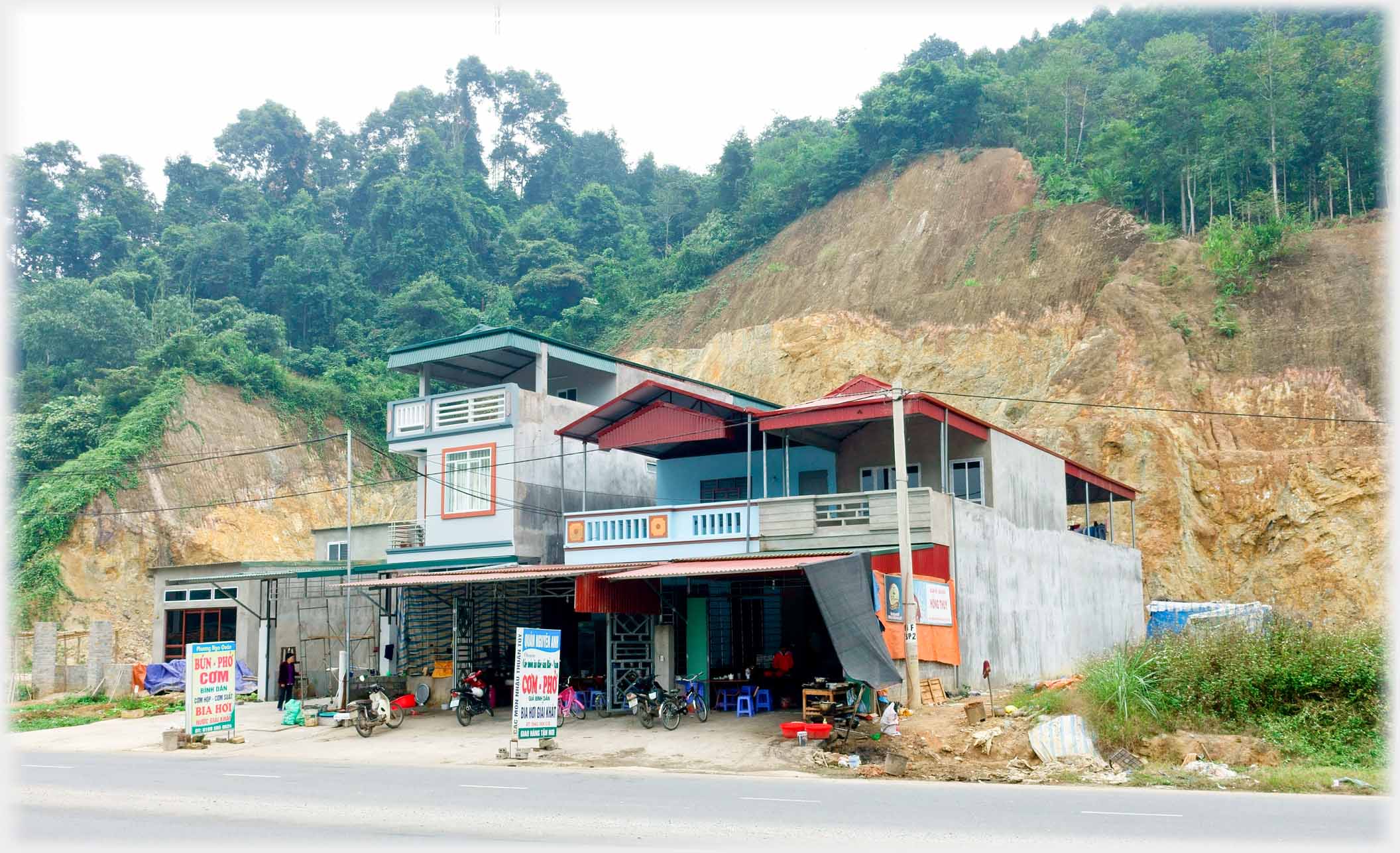 Two story restaurant in excavation from hillside with trees above.