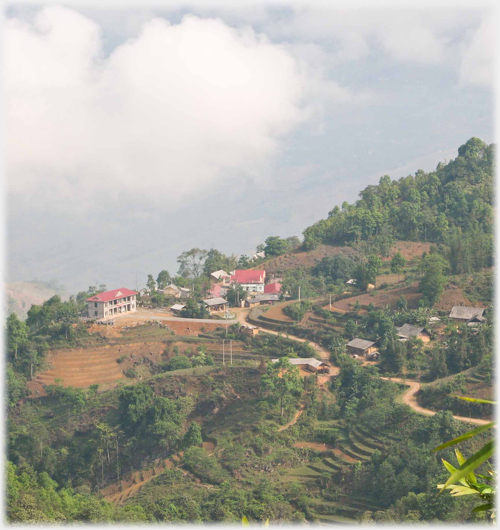 Looking down on winding tracks leading to small group of buildings, clouds below and beyond.